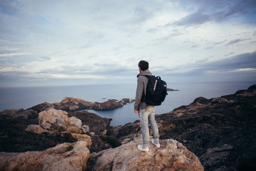 Solo traveler on rocky coast during adventure tour with coastal view.